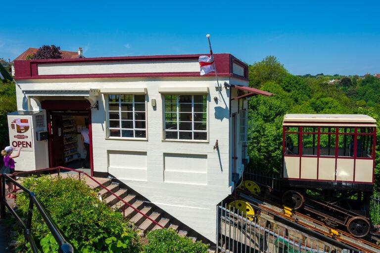 Babbacombe Cliff Railway station building with the car waiting on the track beside railings and greenery on a sunny day.